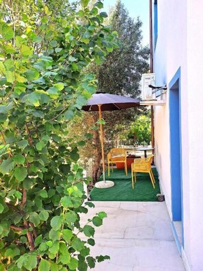 Une terrasse avec une table et des chaises, un petit jardin et la façade d’un bâtiment.