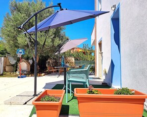 Un espace extérieur aménagé avec une table et des chaises, un panier de basketball et des jardinières fleuries.