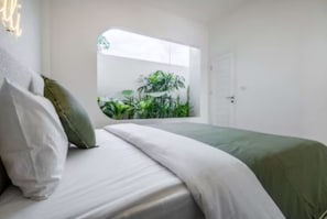 Ein Schlafzimmer mit Bett, Kissen, einem Fenster und Blick auf Grünfläche.