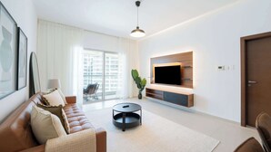 A modern living room with a leather sofa, a round coffee table, a flat-screen TV mounted on a wooden panel, and a large window with a view of buildings. - Modern 1BR Living at Reem Island by Vanilla Homes (Abu Dhabi)