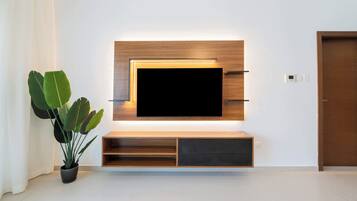 A modern living room with a flat-screen TV mounted on a wooden wall unit, a potted plant, and a closed door.