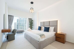 Ein modernes Schlafzimmer mit einem großen Bett, Nachttischen, einem Sessel und Blick auf die Stadt.