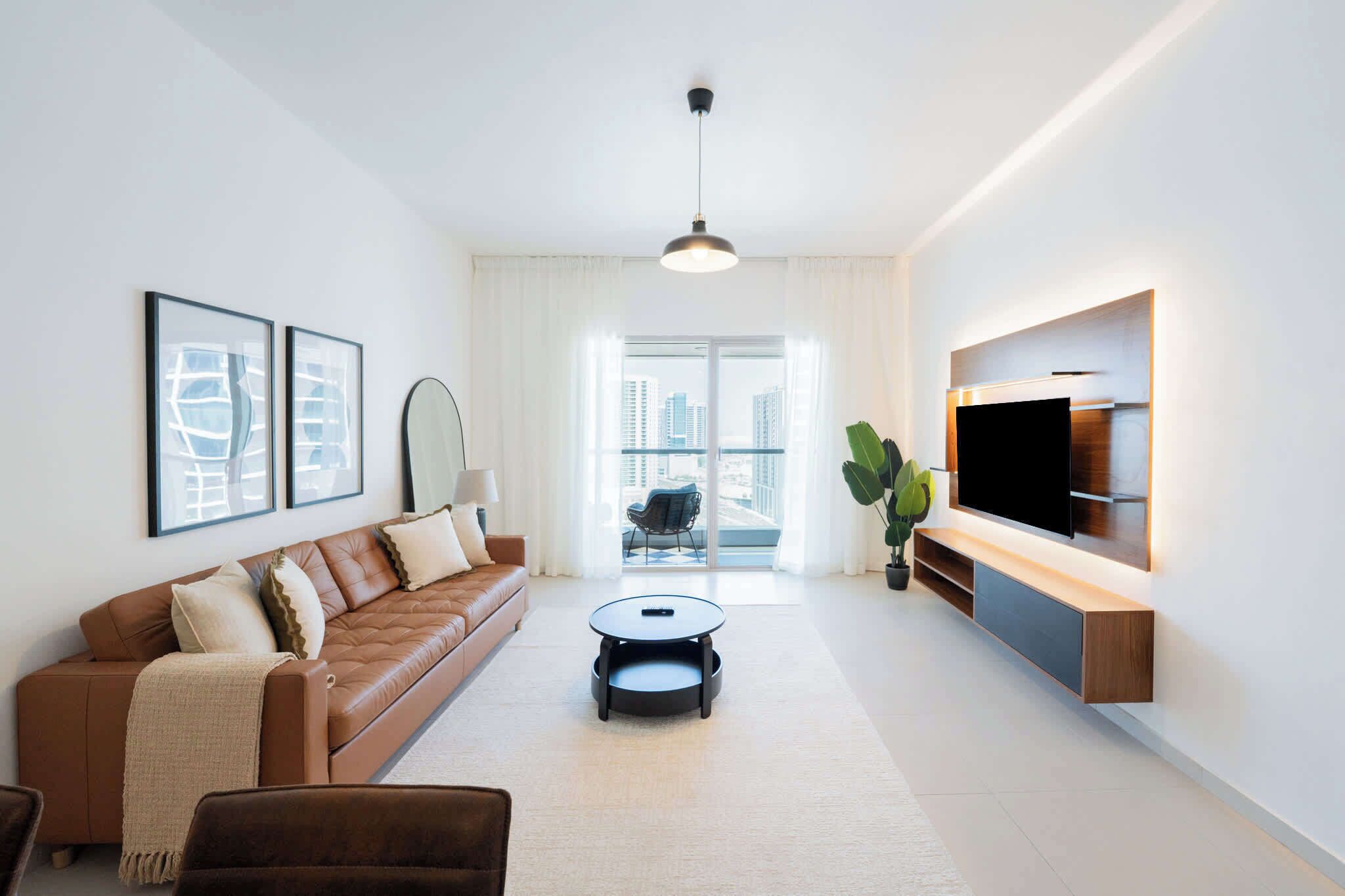 Een moderne woonkamer met een bruine leren bank, een ronde salontafel en een flatscreen televisie aan de muur.