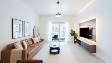 Een moderne woonkamer met een bruine leren bank, een ronde salontafel en een flatscreen televisie aan de muur.