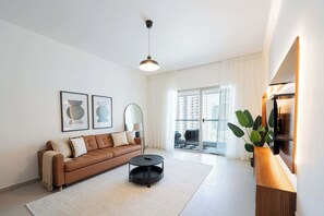 Ett modernt vardagsrum med en brun lädersoffa, ett runt svart soffbord och ett stort fönster med gardiner.