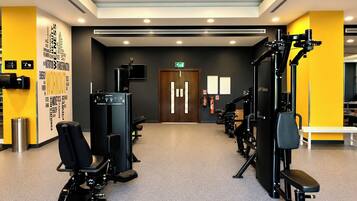 Een sportschool met fitnessapparatuur, een muur met motiverende woorden en een deur met nooduitgangsborden.