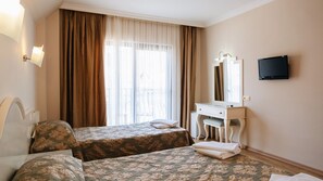 Habitación de hotel con dos camas, un tocador con espejo, televisión y ventana con cortinas.