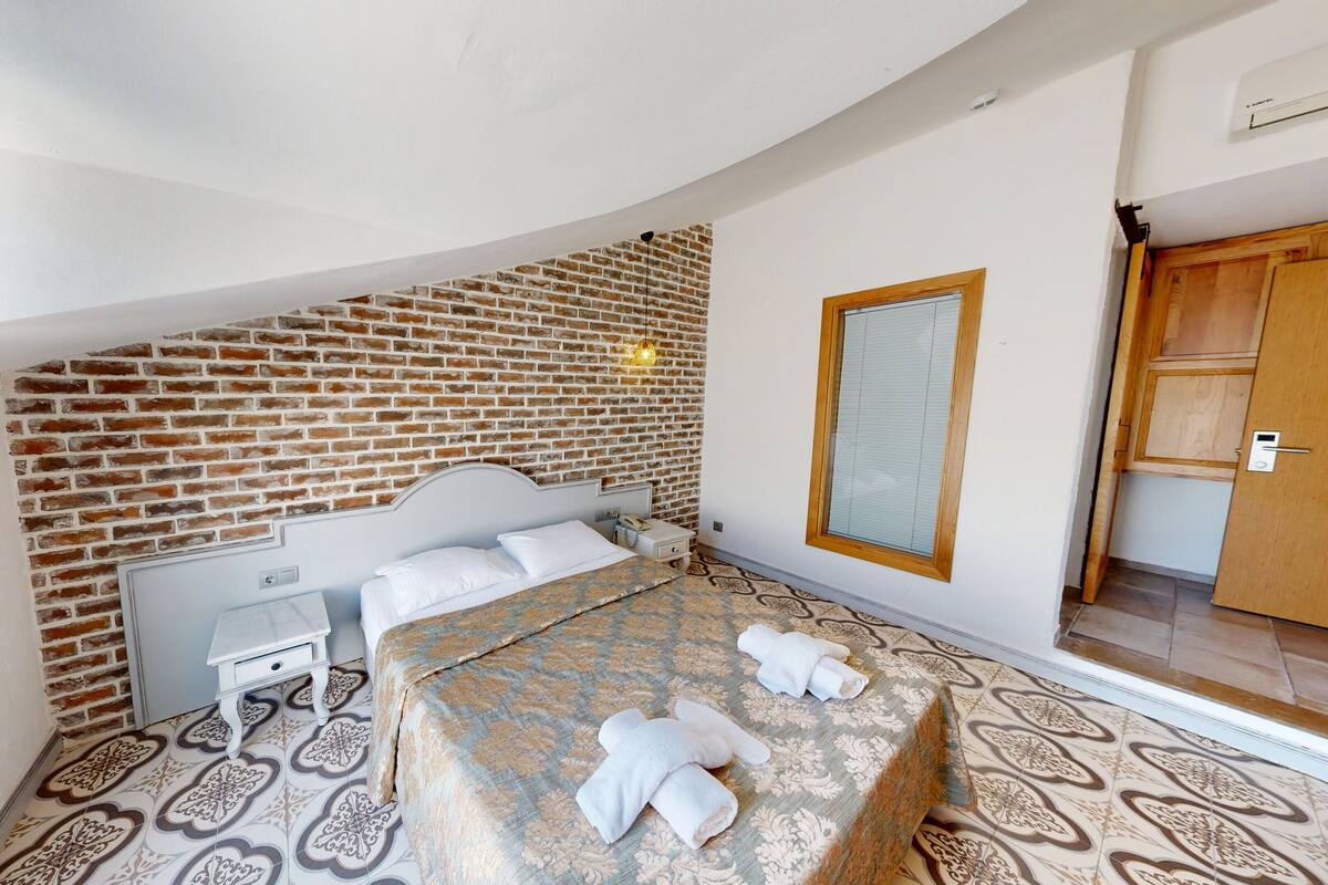 A bedroom with a brick wall, a bed with a patterned bedspread, a bedside table, and a nightstand.