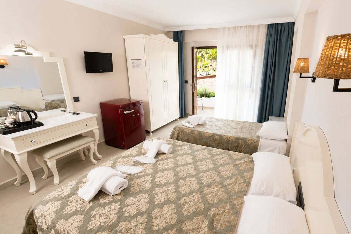A hotel room with two beds, a desk, a wardrobe, a television, and a window with curtains.