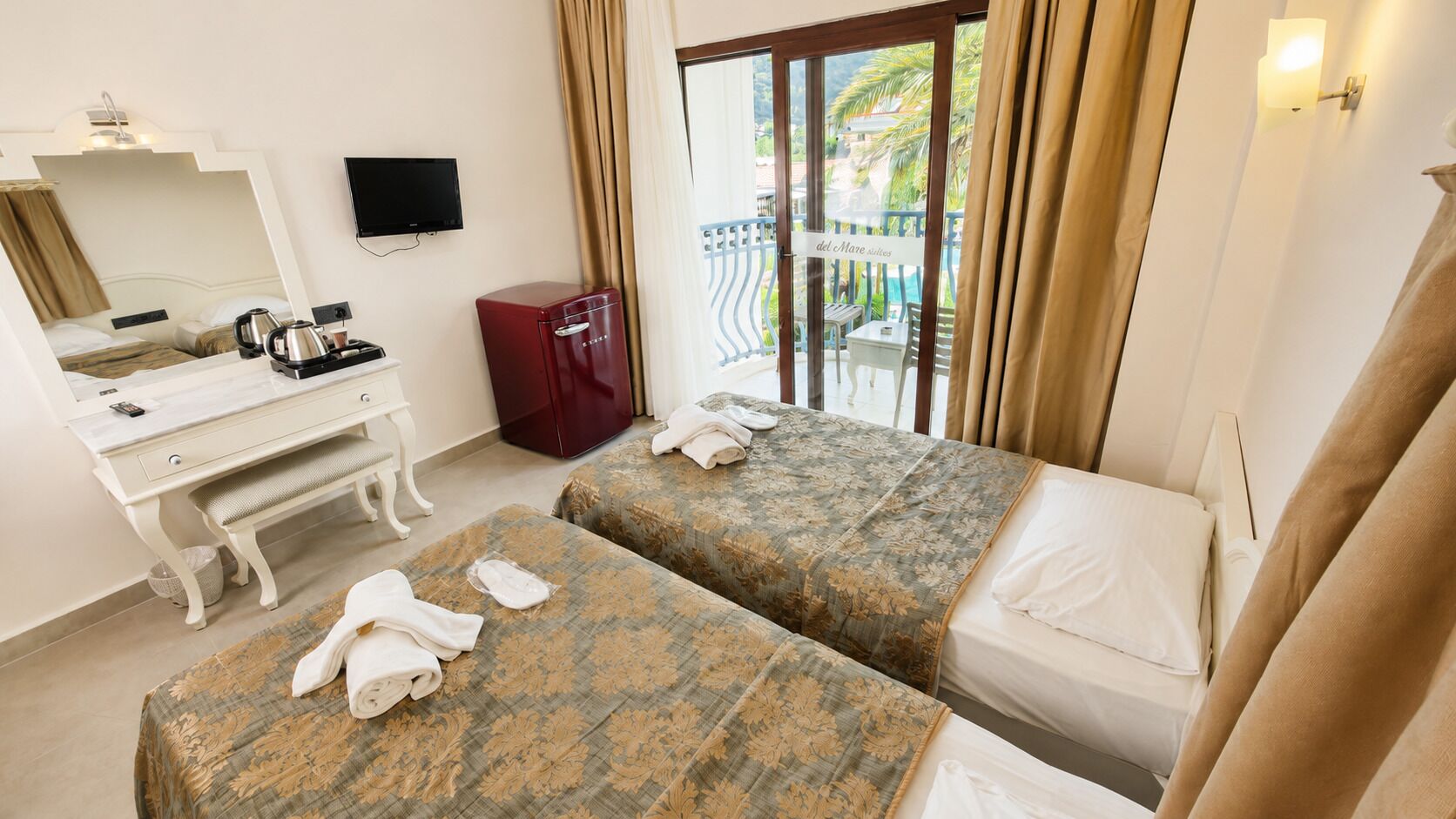 Ein Hotelzimmer mit zwei Betten, einem Schreibtisch mit Stuhl, einem roten Schrank, einem Fernseher und einem Balkon mit Blick.