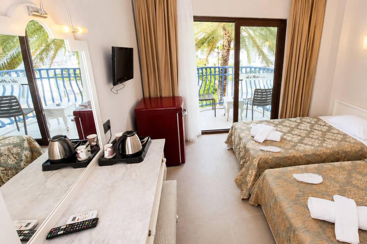 A hotel room with two beds, a dining table with tea set, a red refrigerator, and a TV mounted on the wall.