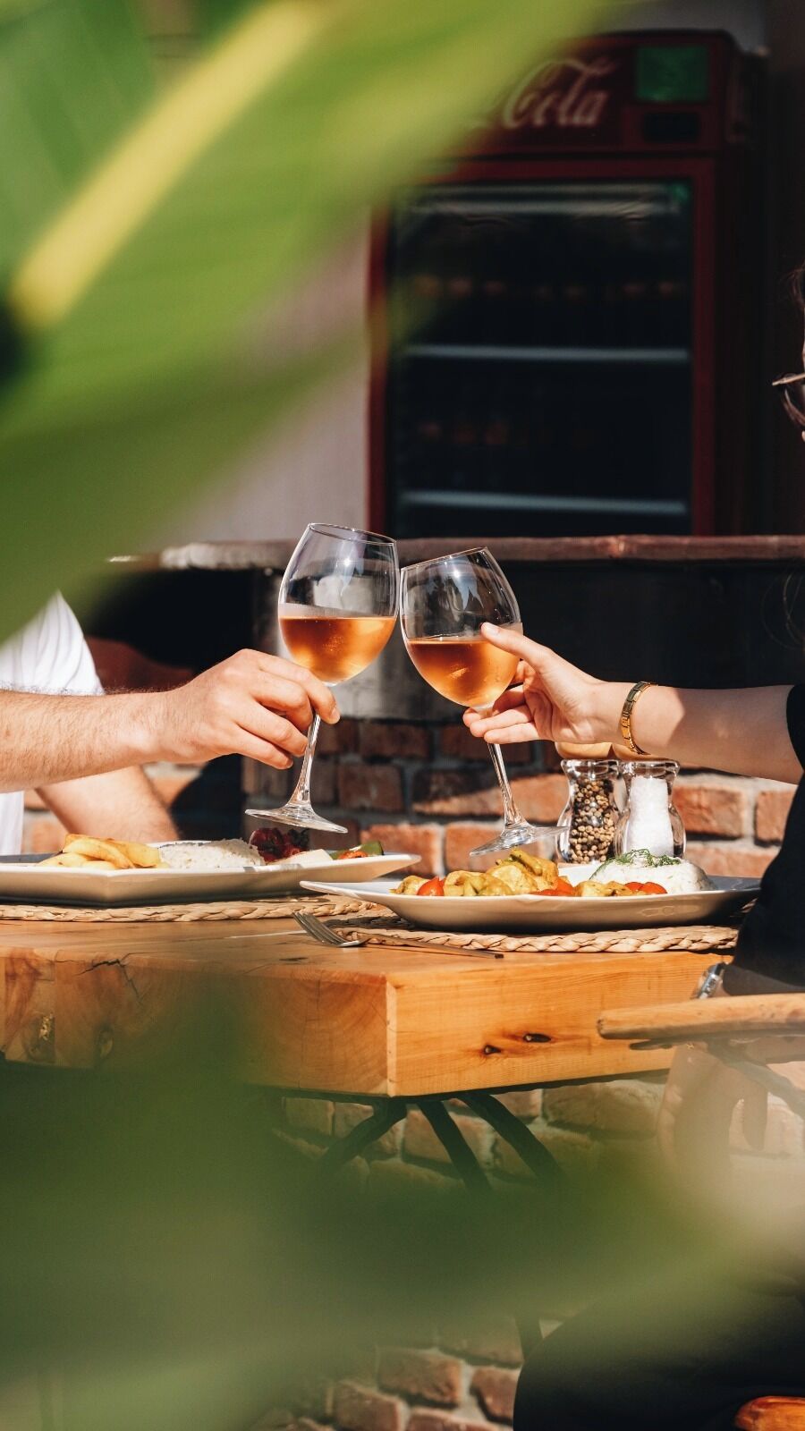 Dos personas brindando con copas de vino en una mesa de madera con platos de comida.