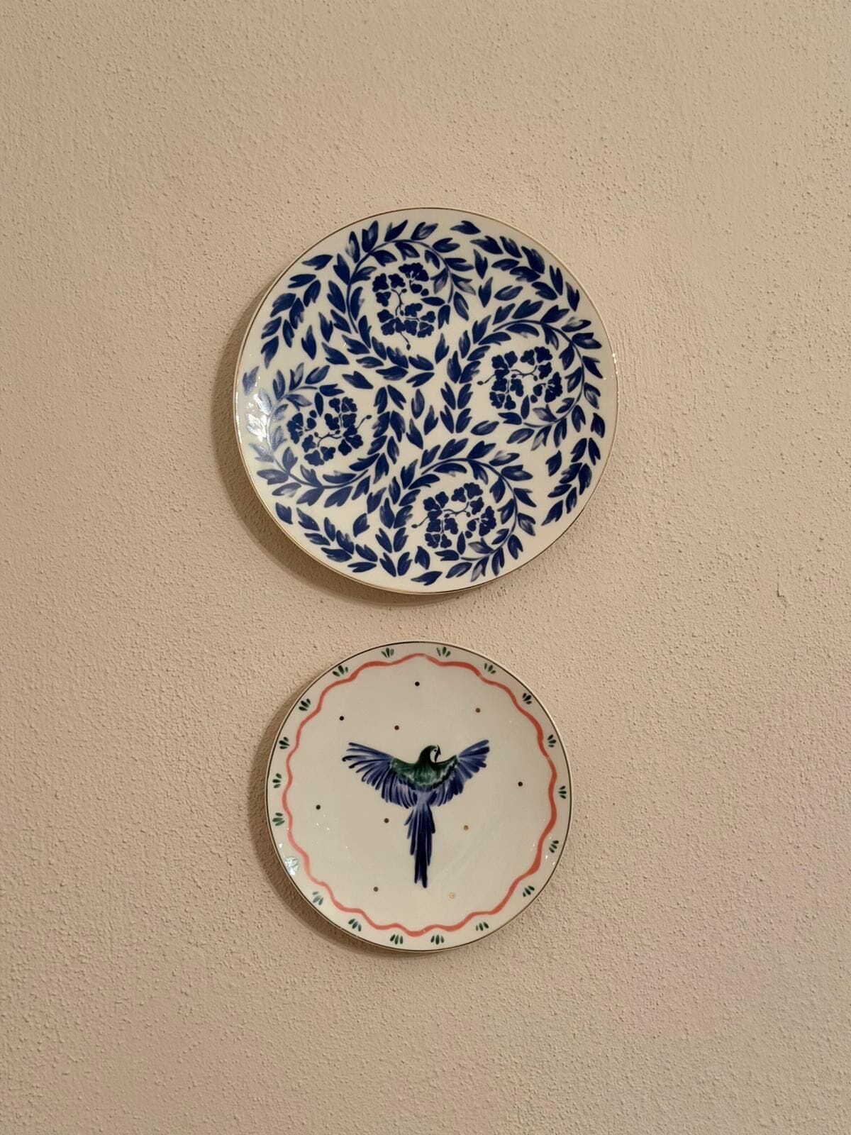 Two plates with floral and avian designs on a plain wall.