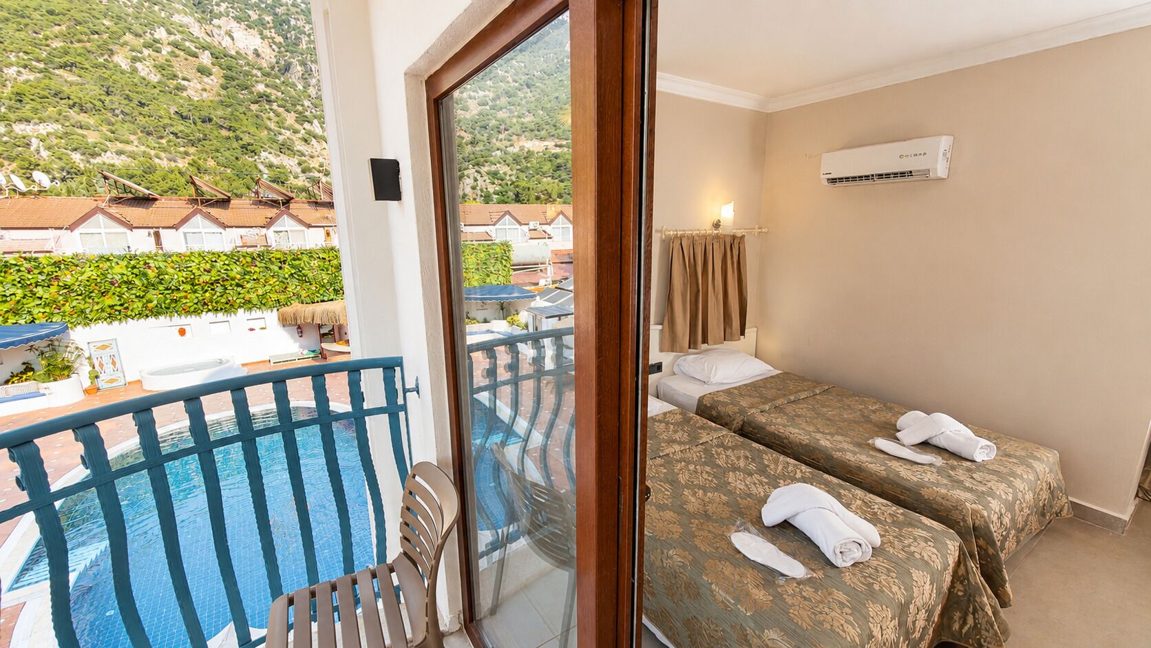 A hotel room with a balcony, two beds, a pool, and a view of houses.