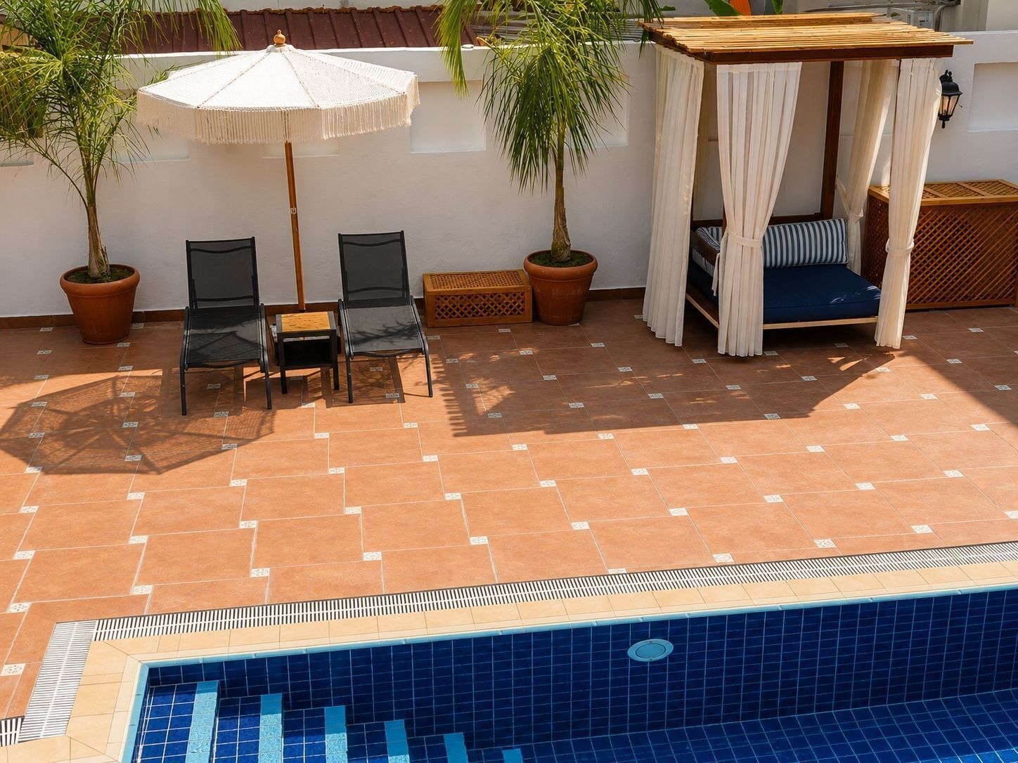 A poolside area with a seating arrangement, a pergola, and potted plants.