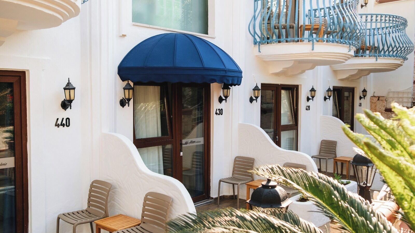 A hotel with outdoor seating, numbered doors, and a blue awning.