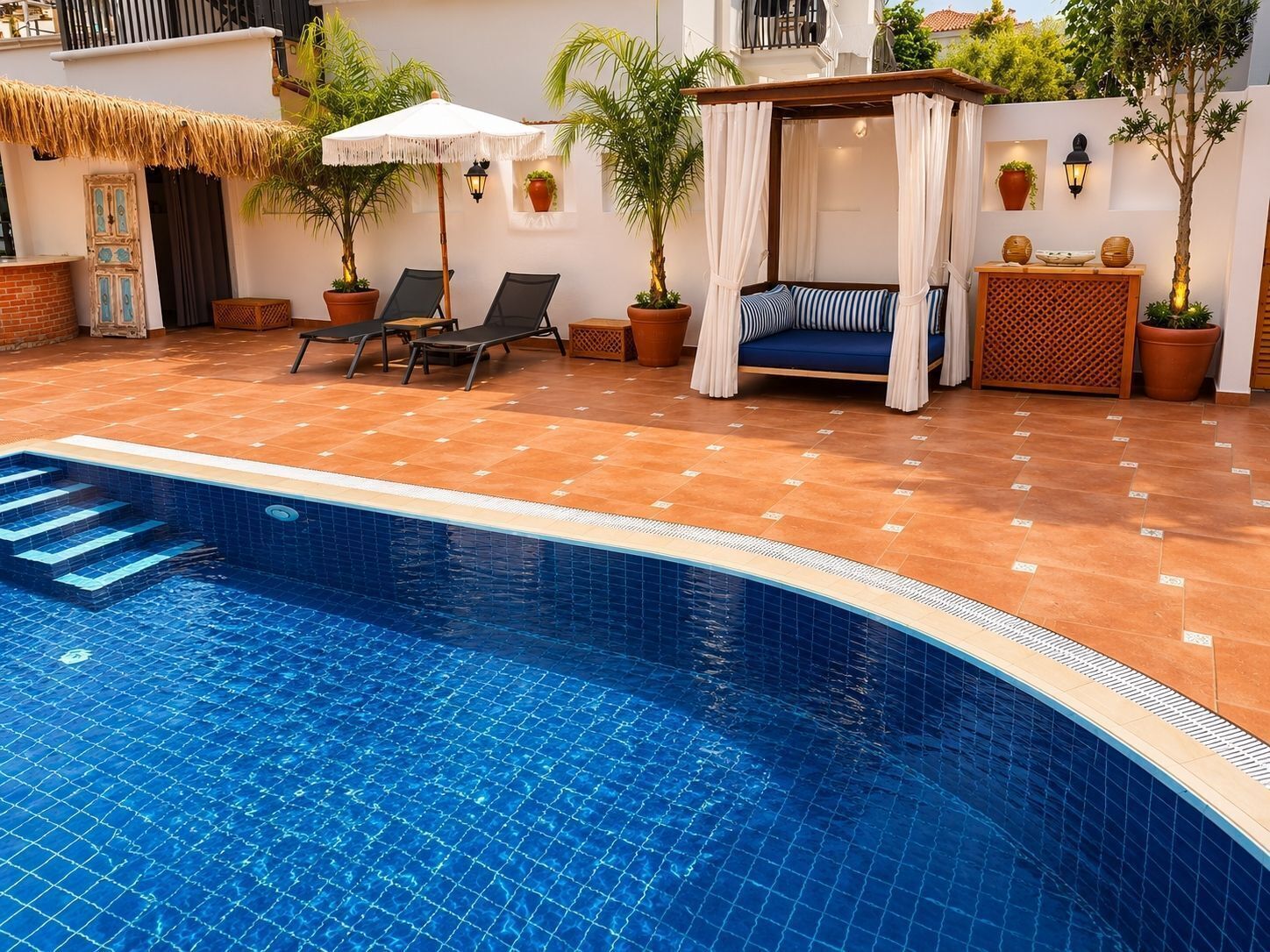 Une piscine dotée de chaises longues et de fauteuils, entourée de plantes en pot et agrémentée d’une pergola surmontée d’un auvent blanc.