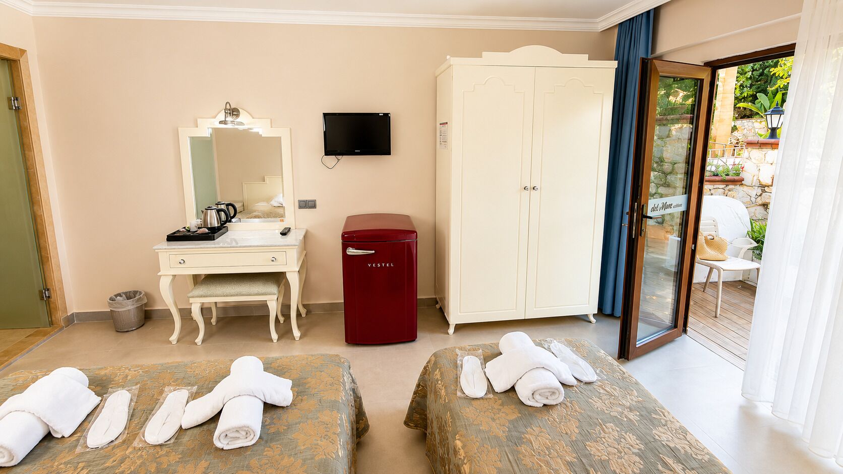 A hotel room with a desk, a television, a wardrobe, a minibar, and two beds with towels.