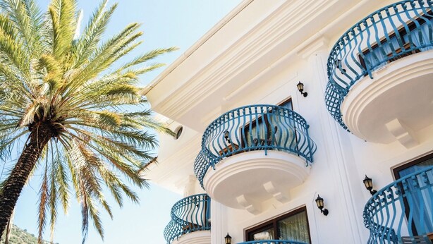 A building with multiple balconies, a palm tree, and a clear sky. - del Mare Hotel Ölüdeniz (Fethiye)