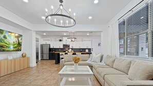 Ein modernes Wohnzimmer mit Glastisch, beiger Couch und einer Küche im Hintergrund.