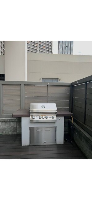 Ein Grill mit integriertem Schrank steht auf einer Holzterrasse mit Blick auf ein Gebäude im Hintergrund.