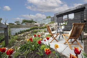 Eine Terrasse mit zwei Holzstühlen, einem Tisch und einer Steinmauer.