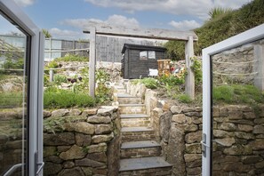 Eine Steintreppe führt zu einer Holzhütte mit Blick auf einen Garten.