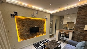 A modern living room with a fireplace, a flat-screen TV, and a dining area with a kitchen in the background. - Nova Park Suites (İstanbul)
