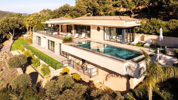 Ein modernes Haus mit Swimmingpool, einer Terrasse mit Liegestühlen und Blick auf den umliegenden Wald.