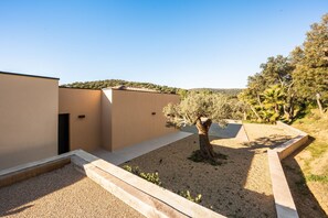 A modern building with a flat roof, a gravel courtyard, and a tree. - Luxury Villa Arizona - Sea View (Grimaud)