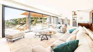Ein modernes Wohnzimmer mit einer großen Glaswand, einer Sofagarnitur, einem Couchtisch und Blick auf eine Hügellandschaft.