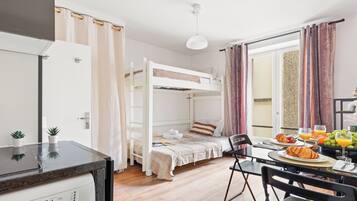 A room with a bunk bed, a dining table with breakfast, and a view through a window.