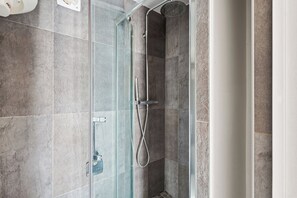 A glass-enclosed shower with a handheld showerhead and a wall-mounted faucet. - Studio Near Eiffel & Musée d'Orsay (Paris)