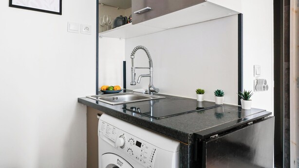 A compact kitchen with a built-in dishwasher, a stainless steel sink, and a black countertop. - Studio Near Eiffel & Musée d'Orsay (Paris)