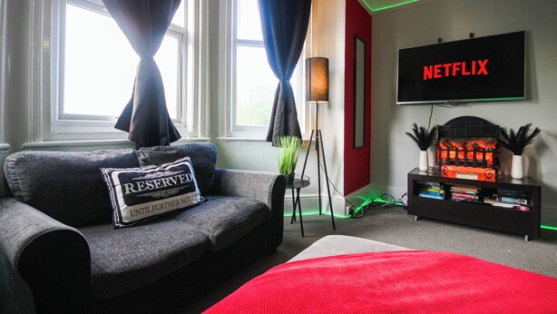 A modern living room with a sofa, a red rug, a fireplace, and a TV displaying 'NETFLIX'. - Aura - Sleeps 6 - Free Parking (Folkestone)