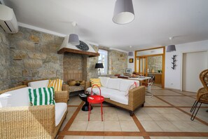 A living room with a stone wall, wicker furniture, a red side table, and a kitchen in the background. - Bella Vista Vrsar - Rustic Apt /w Sea View Balcony (Vrsar)