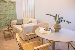 A room with a sofa, a round table with a magazine, a wicker chair, a small side table, and a potted plant. - 4Duques Apartments (Cáceres)