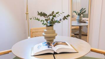 A round table with an open book, a potted plant, and wicker chairs in a room with a mirror and a floor lamp.