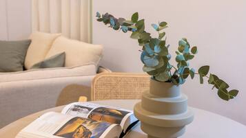 Una habitación con un sofá blanco, una mesita redonda con un libro y un jarrón de hojas verdes.