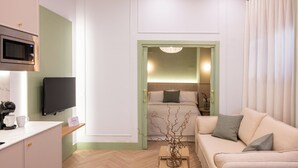 Een moderne hotelkamer met kitchenette, flatscreen-televisie, bed met groene hoofdbord, een bank en een kleine tafel met vaas.