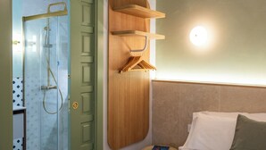 Een hotelkamer met een bed, een houten plank, een nachtkastje, een wandlamp en een douche.