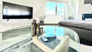 Una sala moderna con un televisor de pantalla plana, una mesa de centro de vidrio, un sofá y una cama.