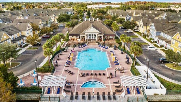 A residential area with a central swimming pool surrounded by lounge chairs and umbrellas, with houses in the background. - Kissimmee 4BR l Resort Living l Great Location (Kissimmee)