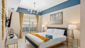A bedroom with a bed, bedside lamps, a desk, a chair, a TV, and a window with curtains. - Kissimmee 4BR l Resort Living l Great Location (Kissimmee)