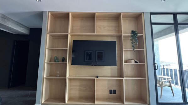 A modern living room with a large TV, wooden shelving, and a balcony view. - w Well-appointed 2BR w Balcony in Tabacalera (Mexico City)