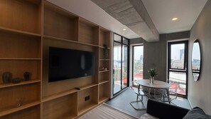 A modern living room with a large TV, wooden shelving, a dining area with chairs, and large windows offering city views. - w Well-appointed 2BR w Balcony in Tabacalera (Mexico City)