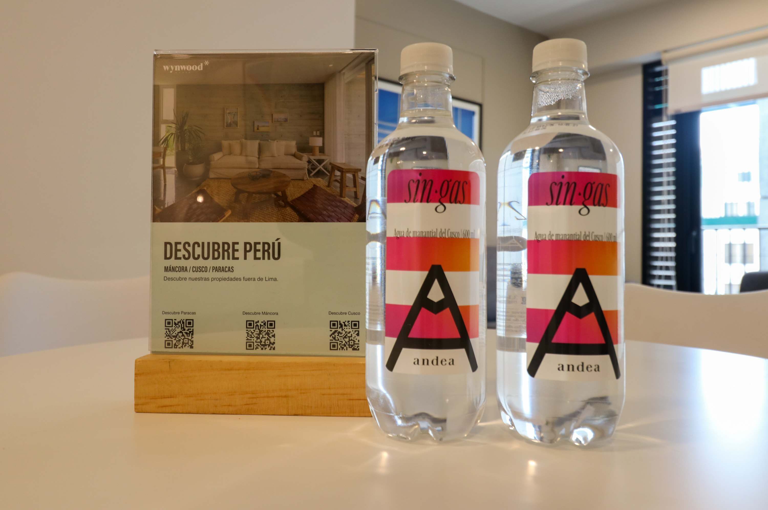 Zwei Flaschen 'sin-gas' Wasser, ein QR-Code und eine Broschüre mit dem Titel 'DESCUBRE PERÚ' auf einem Tisch.