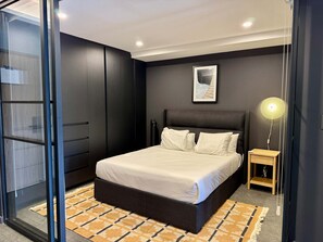 Ein modernes Schlafzimmer mit einem großen Bett, einem Nachttisch, einer Stehlampe und einem gerahmten Bild an der Wand.