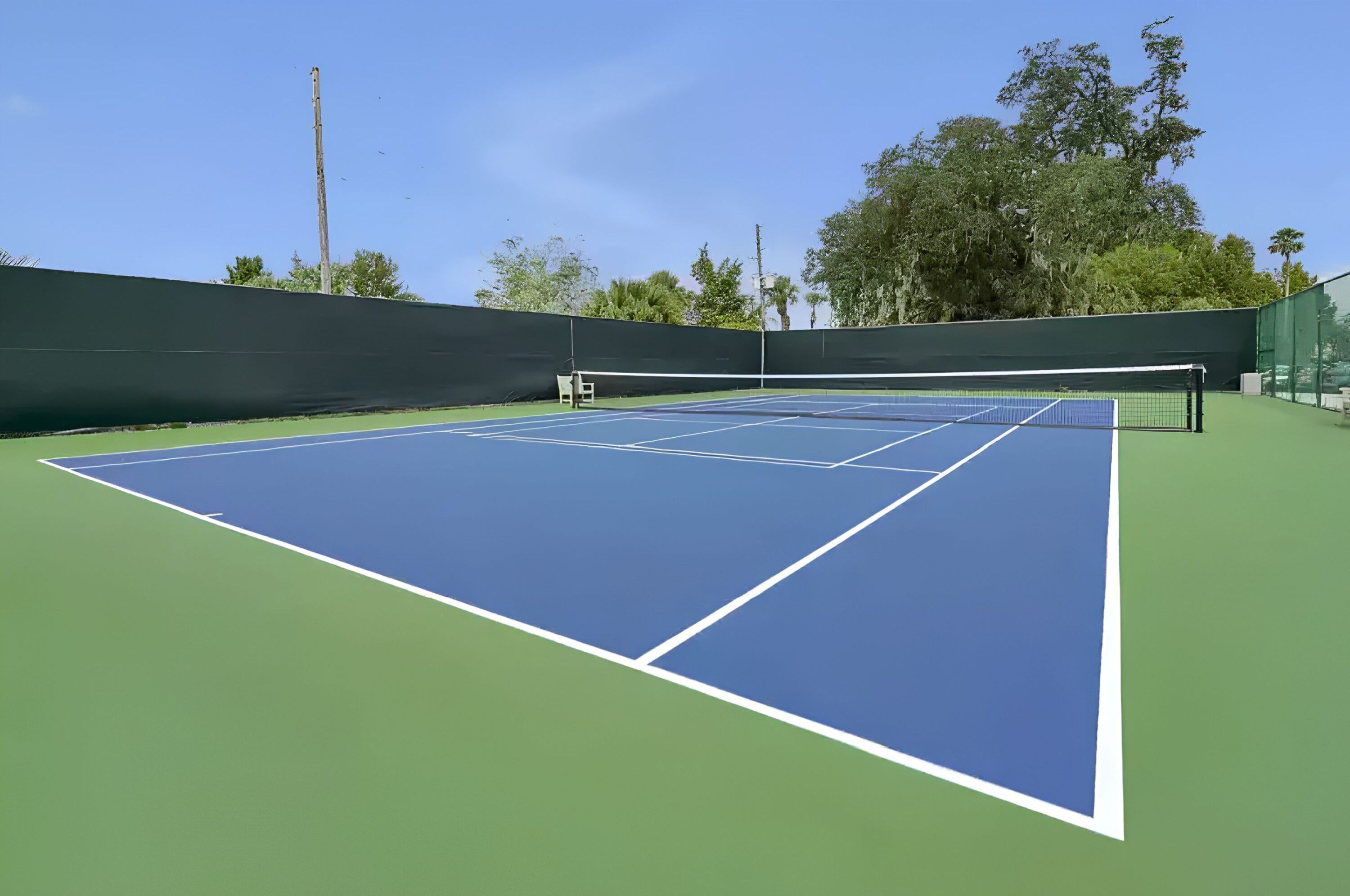 A tennis court with a net, green and blue playing surfaces, and trees in the background.