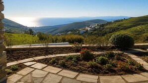 A garden with stone pathways, a view of the sea, and a hillside with buildings. - Tzados Sunny Villa - Tinos Summer Retreat (Tinos)
